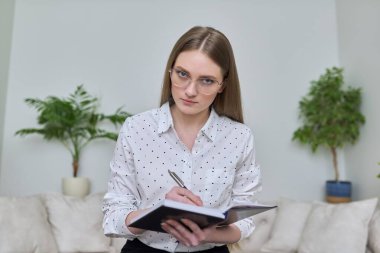 İş defteri olan genç iş kadını webcam 'e bakıyor.