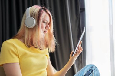 Kulaklıklı genç kız dijital tablet ekranına bakıyor.