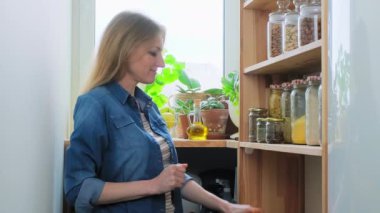 Kilerde yiyecek depoluyor, portakallı orta yaşlı kadın, bir kutu kuru üzüm, bir şişe zeytinyağı.