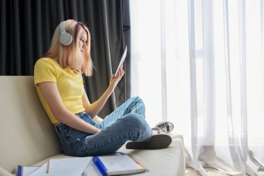 Kulaklıklı genç kız dijital tablet ekranına bakıyor.