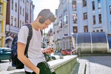 Sırt çantalı kulaklıklı yakışıklı genç akıllı telefon ekranına bakıyor.