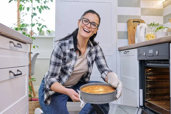 Woman at home in kitchen taking out hot apple pie from oven