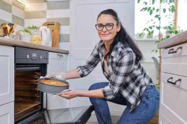 Mutfaktaki kadın sıcak elmalı turtayı fırından çıkarıyor.