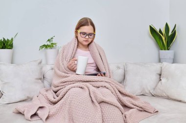 Soğuk sonbahar kış sezonu evde, genç kız battaniyenin altında kanepede oturuyor.