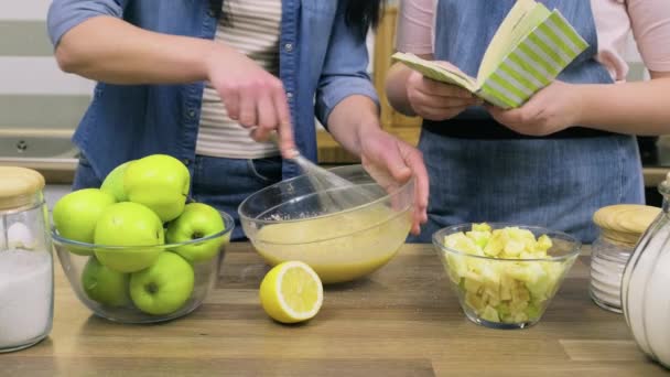 Gros plan des mamans main agitant la pâte et les mains de la fille préadolescente avec livre de recettes — Video