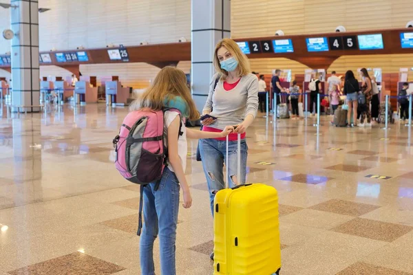 Familia madre e hija niños turistas con maleta en máscaras médicas en la terminal del aeropuerto —  Fotos de Stock