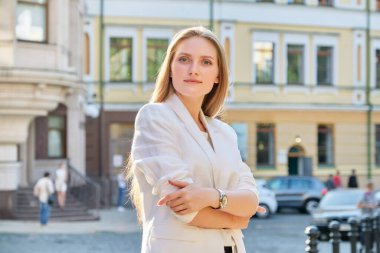 Kollarını kavuşturmuş kendine güvenen genç bir iş kadınının açık hava portresi.