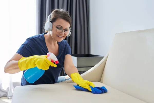 Mujer madura en audífonos guantes con trapo detergente limpieza en casa —  Fotos de Stock