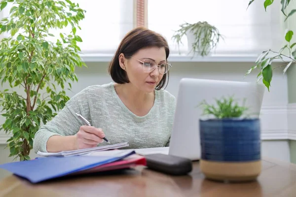 Female teacher teaching online, sitting at home at table with laptop