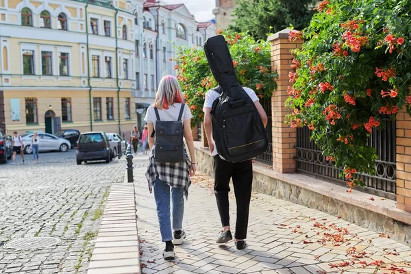 Creative teenagers guy and girl walking with guitar in case, back view — Stock Photo, Image