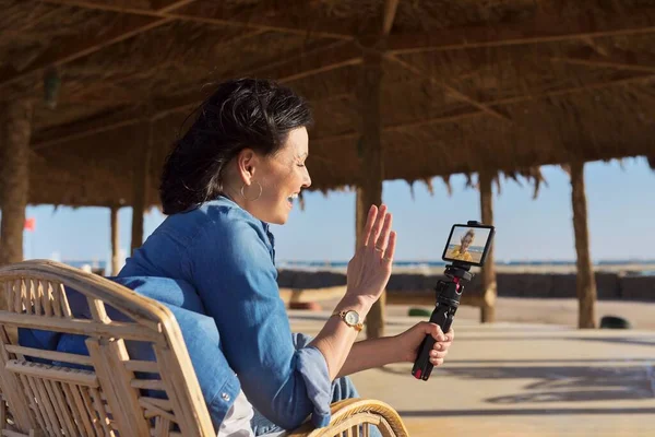 Középkorú nő néz smartphone webkamera beszélő felvétel videó homokos strandon. — Stock Fotó