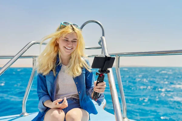 Молода жінка записує потік на смартфон, сидячи на борту яхти в морі — стокове фото