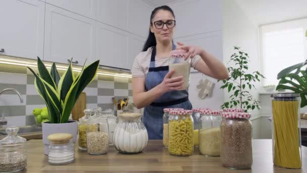 Хранение пищи на кухне, женщина домохозяйка в фартуке с банками и контейнерами — стоковое видео