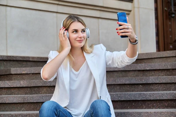 Jeune belle femme dans un casque avec smartphone reposant sur les marches de la ville — Photo