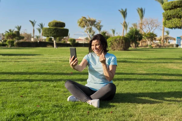 Femme mûre faisant des exercices matinaux sur l'herbe verte dans le parc, avec bouteille d'eau — Photo