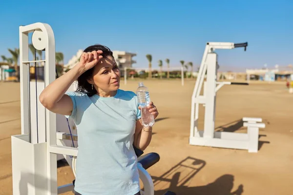 Ώριμη γυναίκα κάνει αθλητική άσκηση σε εξωτερικούς προσομοιωτές, με ένα μπουκάλι νερό — Φωτογραφία Αρχείου