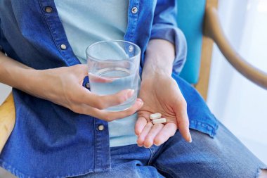 Yetişkin kadınların eli haplarla ve bir bardak suyla yakın plan çekilecek.