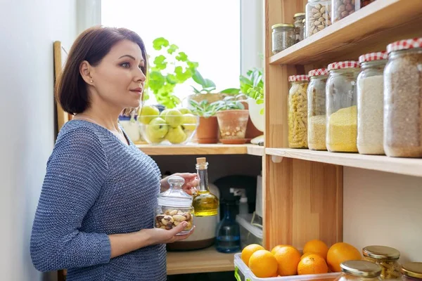 Organisation der Speisekammer, Frau in der Küche in der Nähe von Holzgestell mit Dosen und Behältern mit Lebensmitteln — Stockfoto