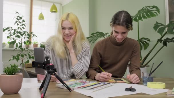 Пара подростков рисуют акварелью вместе, парень и девушка смотрят мастер-класс на смартфоне — стоковое видео