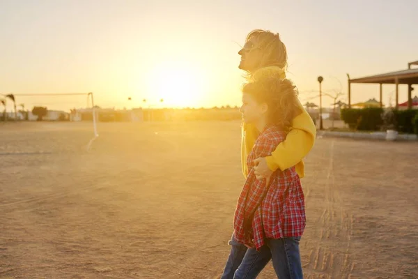 Szczęśliwa matka i córka spacerujące razem przytulające się na zewnątrz, światło zachodu słońca — Zdjęcie stockowe