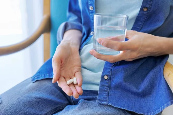 Close-up of mature womans hand with pills and glass of water — Stock Photo, Image