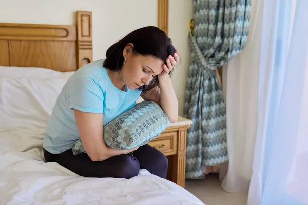 Gammal ledsen lidande kvinna sitter på sängen med kudde — Stockfoto