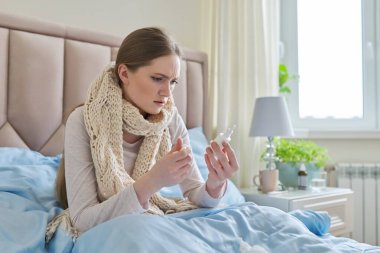 Genç hasta bir kadın, burun damlası ve mendille yatakta oturuyor.