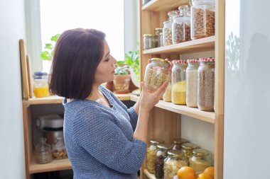 Kiler organizasyonu, mutfaktaki kadın konserve kutuları ve yiyecek kutularıyla ahşap rafın yanında.