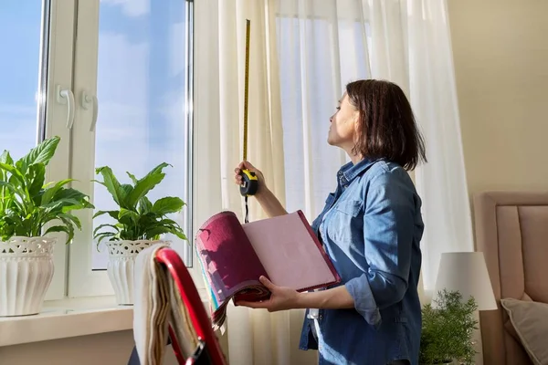 Женщина-дизайнер выбирает ткани для штор, измеряет окно с помощью рулетки — стоковое фото
