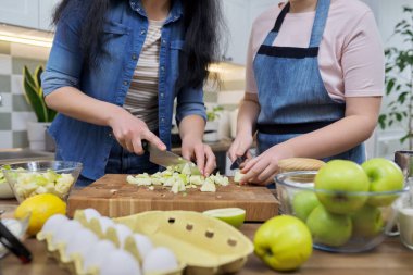 Mutfak tahtasındaki yeşil elmaları kesen anne ve kızın elini kapat.
