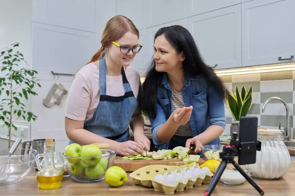 Mãe e filha adolescente cozinhar torta de maçã juntos, olhando para a tela do smartphone — Fotografia de Stock