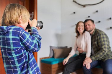 Evde mutlu bir aile, kameralı küçük bir çocuk kucaklaşan ebeveynlerin fotoğrafını çekiyor.