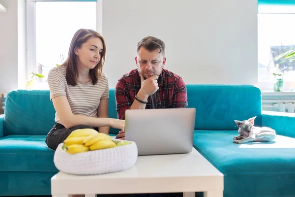 Serieuze middelbare leeftijd paar man en vrouw met laptop zitten thuis op de bank — Stockfoto