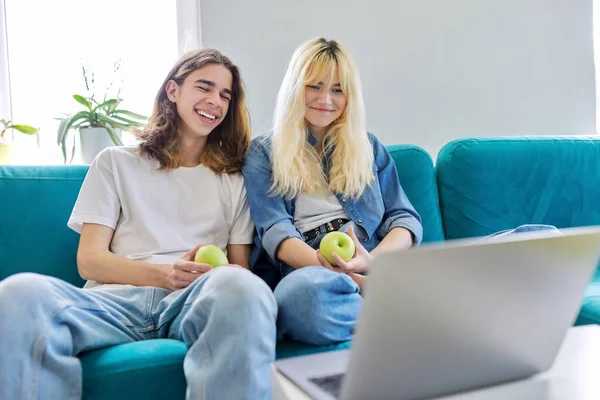 Casal rindo de adolescentes se divertindo, sentados no sofá, olhando para o laptop — Fotografia de Stock