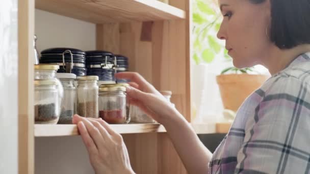 Cucina, dispensa, deposito di cibo, una donna guarda e raccoglie vasi di cibo, spezie, cereali — Video Stock