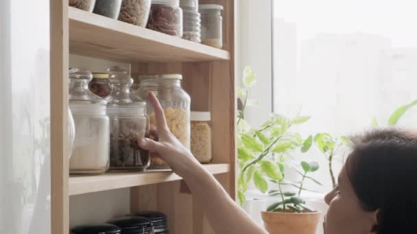厨房，食品室，食品储藏室，一个女人看着并捡起一罐罐罐的食物，香料，谷物 — 图库视频影像