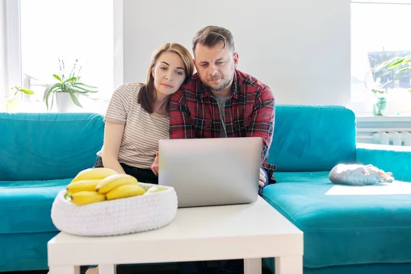 Sério casal de meia-idade marido e mulher com laptop sentado em casa no sofá — Fotografia de Stock