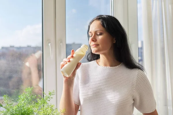 Mulher bebendo bebida de leite de garrafa de pé perto da janela, leite iogurte laticínios bebidas saudáveis — Fotografia de Stock