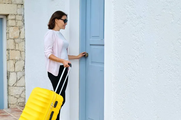 На улице женщина с желтым чемоданом открывает закрывающуюся дверь дома — стоковое фото