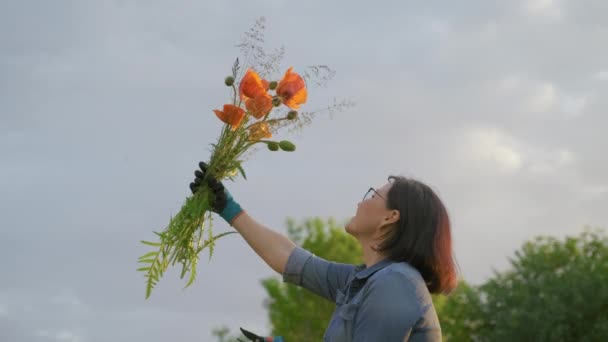 Mujer de mediana edad con un ramo de amapolas en la mano, fondo de la naturaleza del cielo — Vídeo de stock
