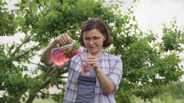 中年の女性がイチゴとミントと自然飲料を注ぐからジャグにガラス — ストック動画