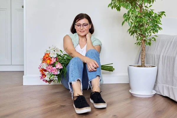 Улыбающаяся женщина средних лет с букетом цветов, сидящих на полу дома — стоковое фото
