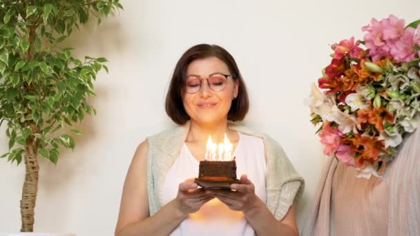 Ältere schöne Frau mit kleiner Geburtstagstorte mit brennenden Kerzen — Stockvideo