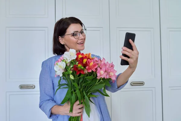 Glückliche Frau mittleren Alters mit großem Blumenstrauß und Smartphone — Stockfoto