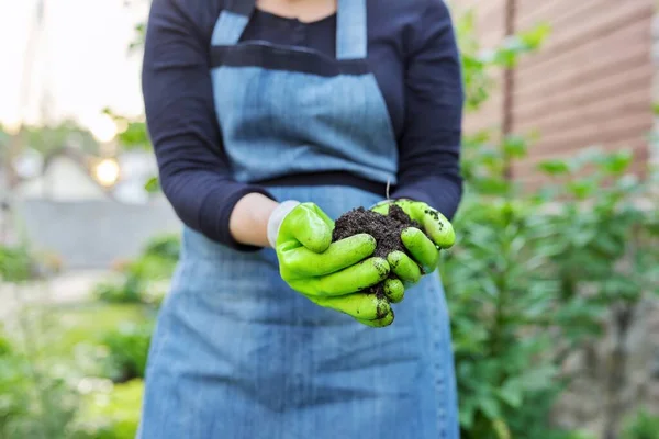 Close-up dari tangan wanita dalam berkebun sarung tangan dengan tanah subur hitam — Stok Foto