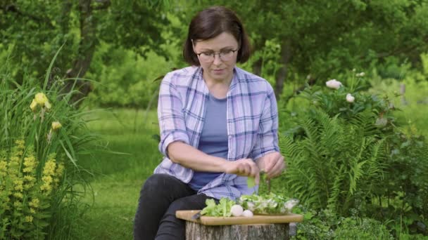 Middelbare vrouw maken van groentesalade in de tuin buiten — Stockvideo