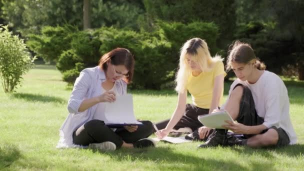 Insegnante di scuola, psicologo, assistente sociale che parla con gli adolescenti, seduto sull'erba — Video Stock