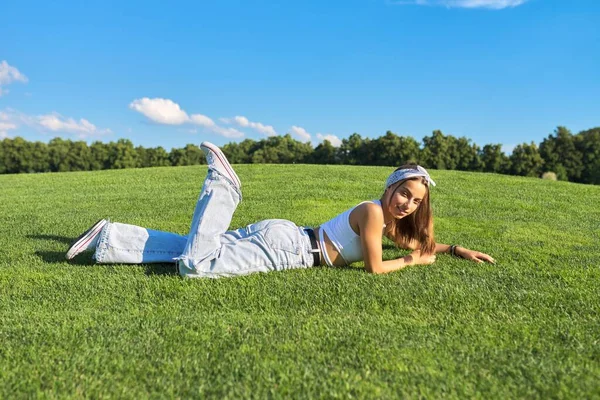 Menina adolescente hipster deitado na grama, gramado verde e fundo céu azul — Fotografia de Stock