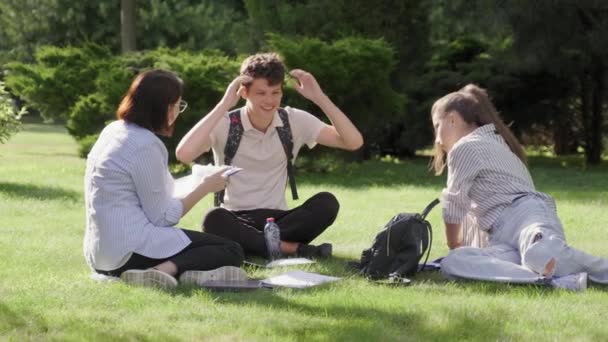 Nauczyciel, psycholog, pracownik socjalny rozmawiający z nastolatkami, siedzący na trawie — Wideo stockowe