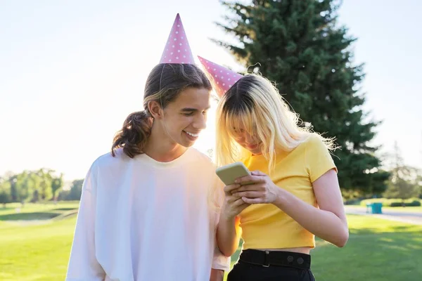 Πάρτυ γενεθλίων, δύο έφηβοι σε καπέλα φεστιβάλ με smartphone εξωτερική — Φωτογραφία Αρχείου